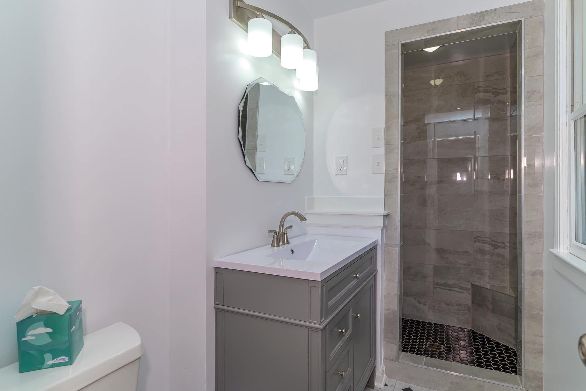 Bathroom vanity with gray cabinet and walk-in tile shower