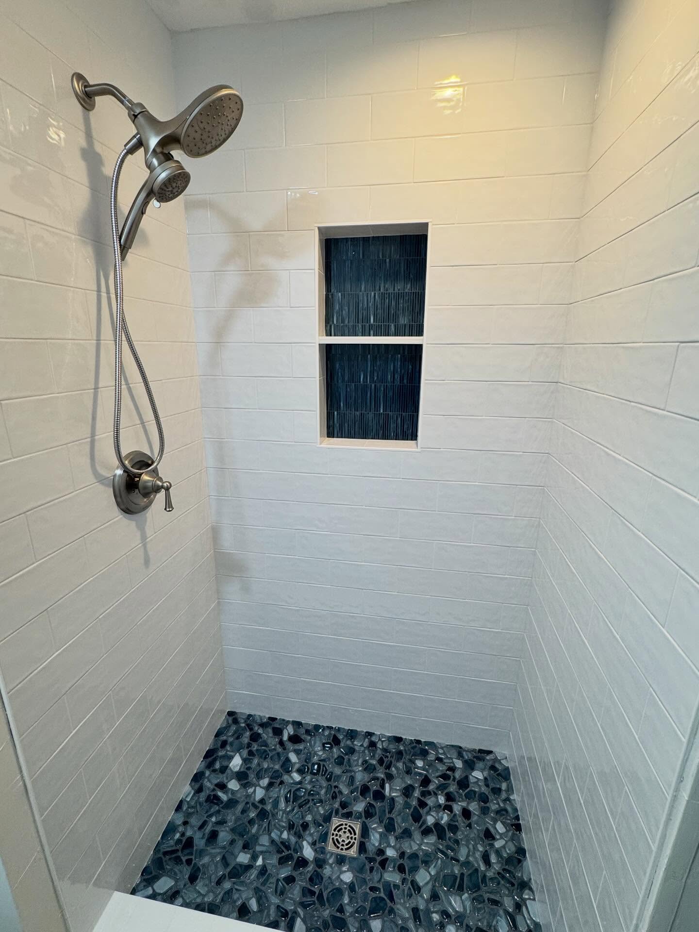 Custom white tile walk-in shower with natural pebble stone floor and glass enclosure
