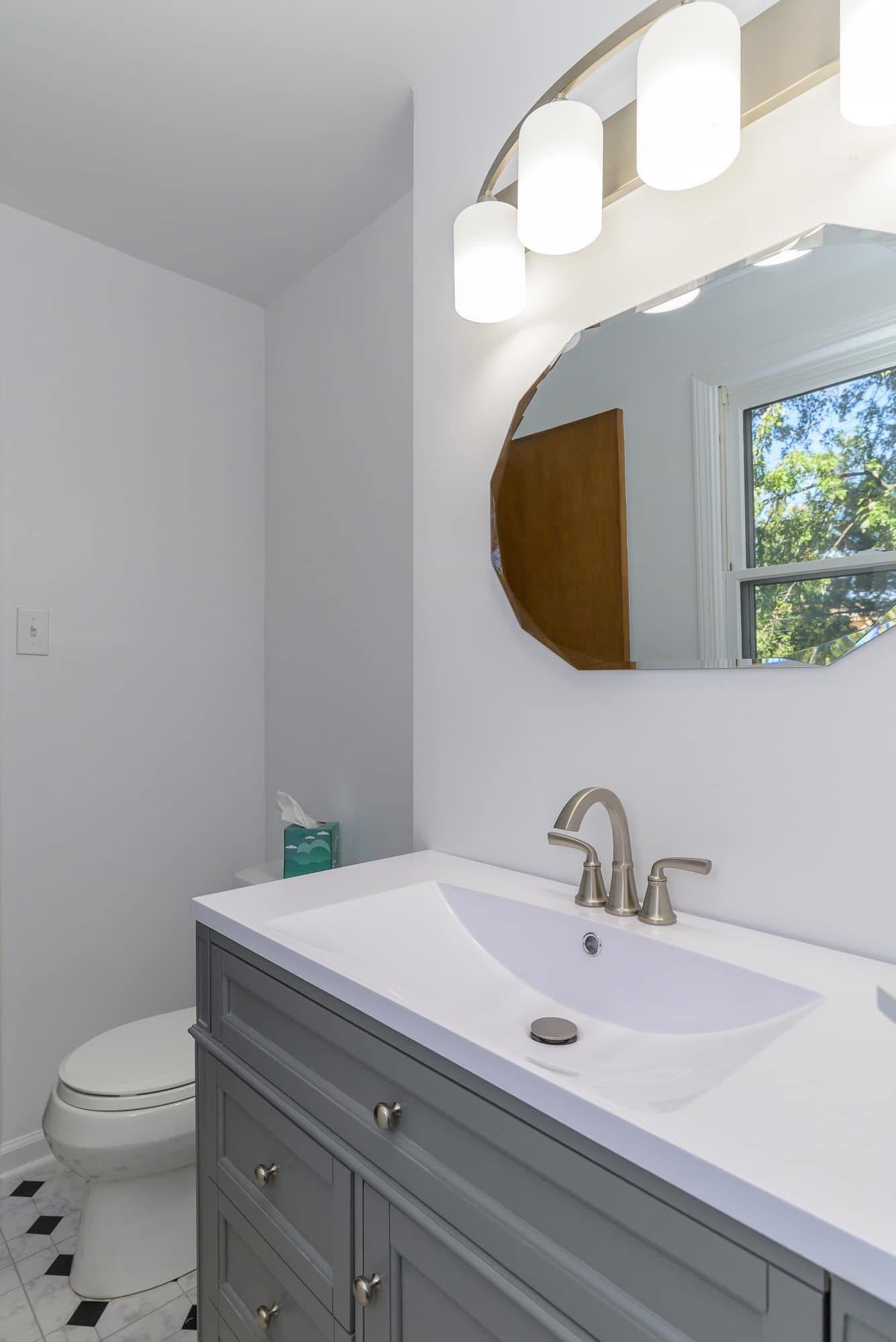 Updated bathroom vanity with gray cabinet and oval mirror