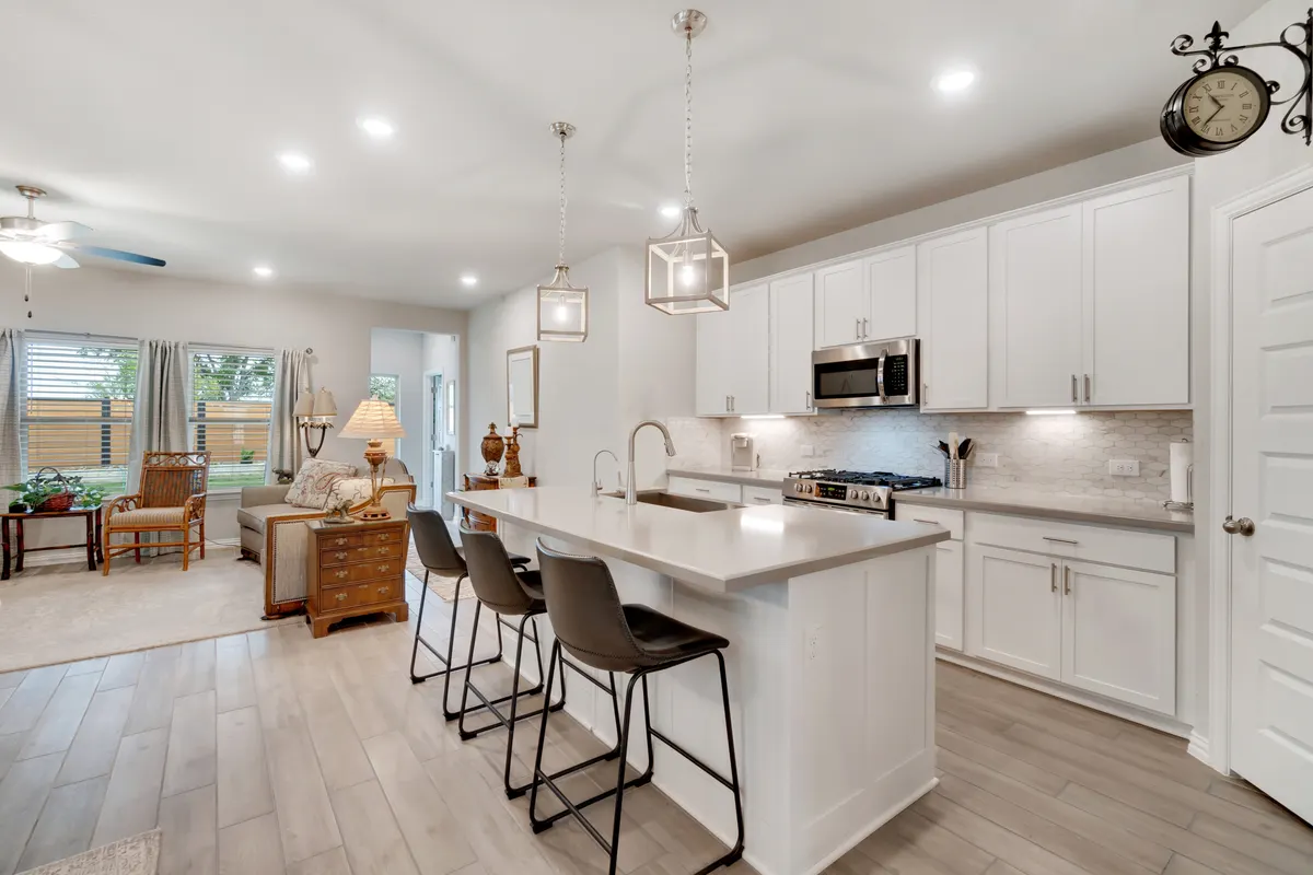Open-concept kitchen remodel with a quartz island, white shaker cabinets, and lantern pendants opening to the living room