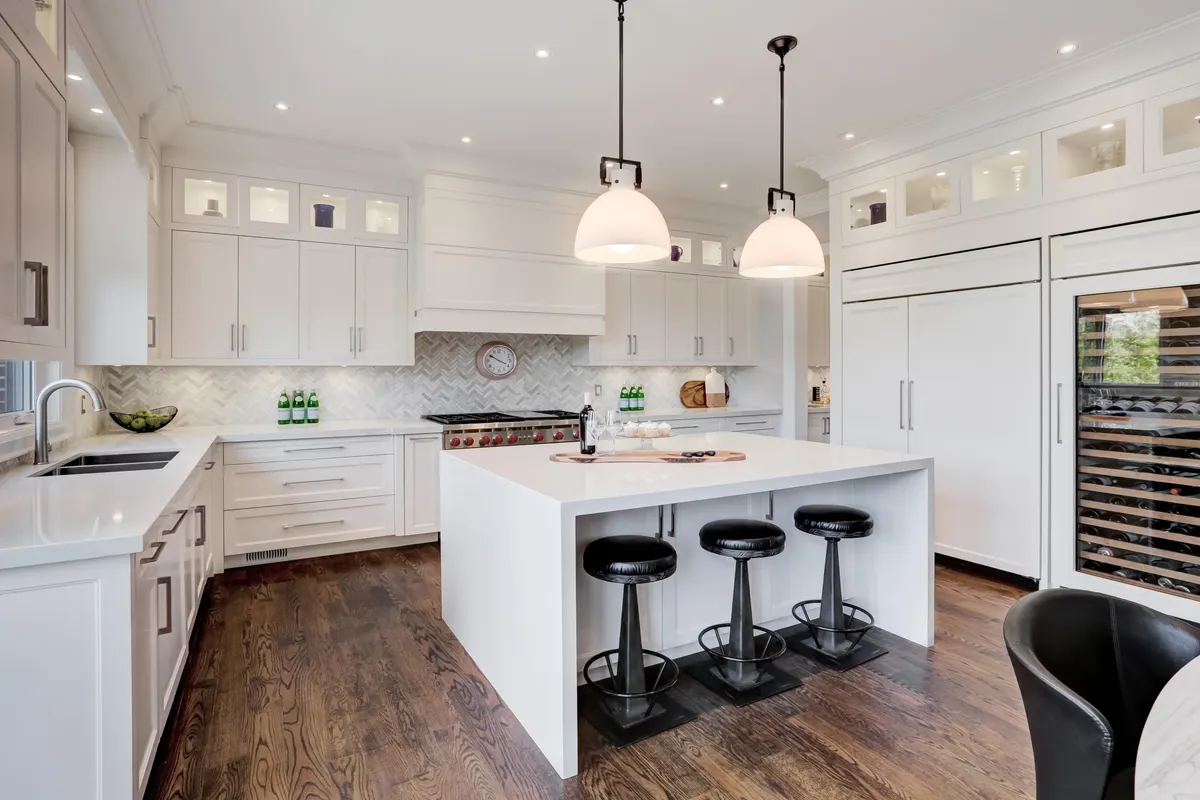 Bright white kitchen remodel with a quartz waterfall island, herringbone backsplash, and pendant lighting