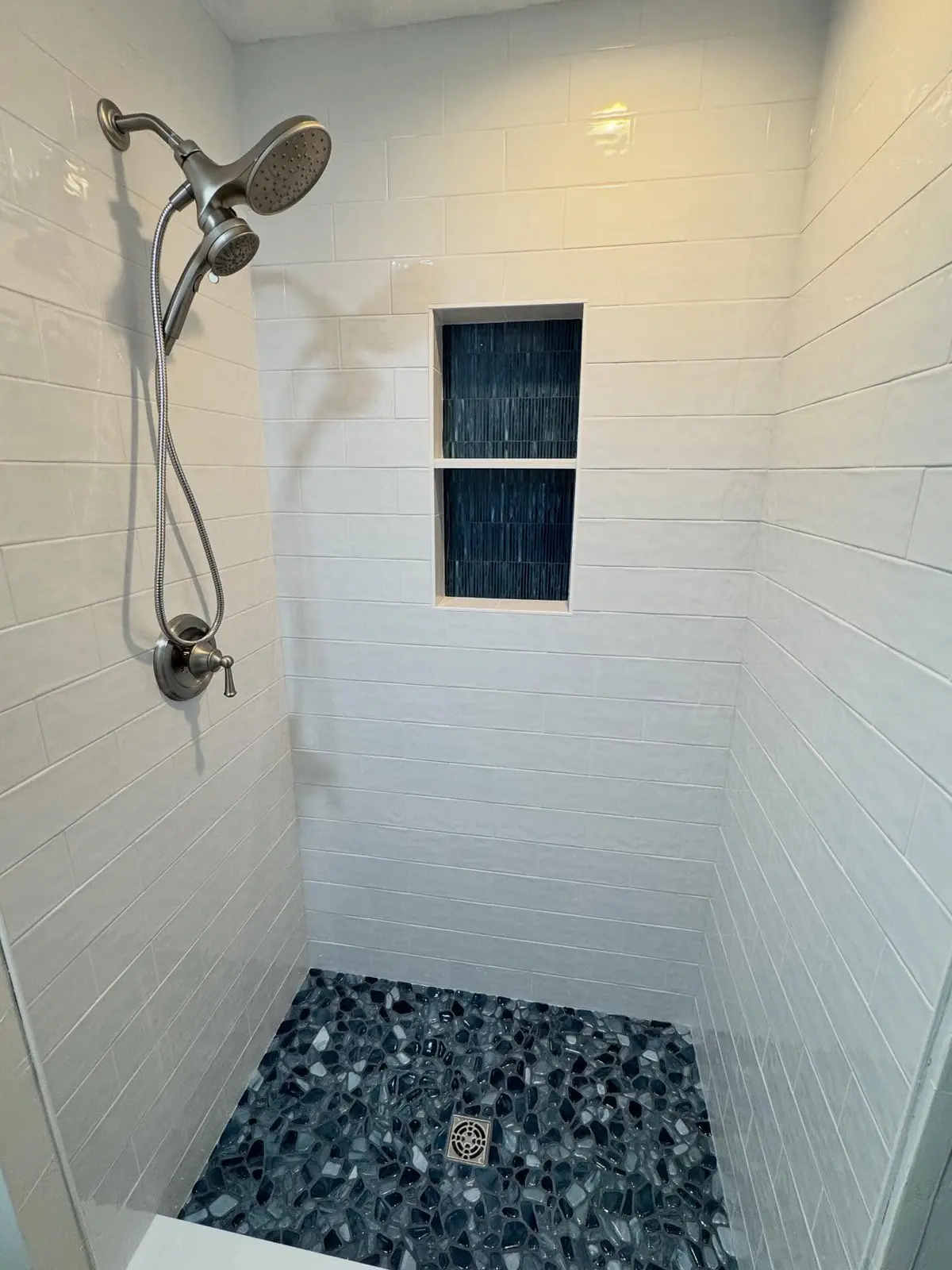 Finished walk-in shower with white subway tile and pebble stone floor